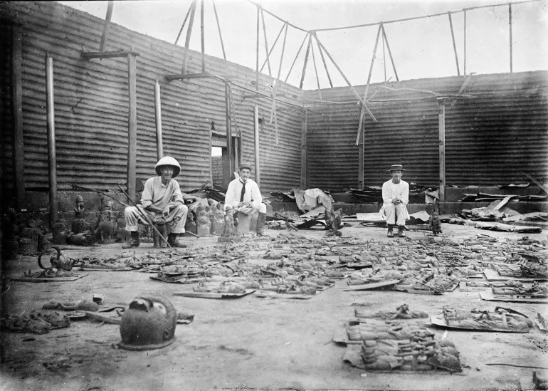 The interior of the Benin king’s compound burned during the siege of Benin city in 1897, with stolen treasures of africa, especially bronze plaques in the foreground [Photographer Reginald Granville Wikimedia Commons]
